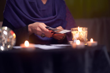 Close-up of fortune teller female divining on cards sitting at table with burning candles, magic ball