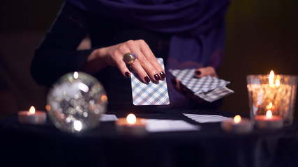 Close-up of fortuneteller hands with cards while sitting at table with candles in dark room