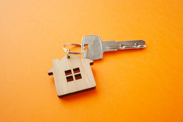 Key and house shaped keychain arrangement on orange background. Top view, flat lay. Real estate,...