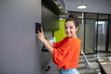 Fototapeta na wymiar Young woman holding tablet against kitchen wall, smiling