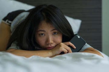 young depressed Asian Korean woman on bed sad and worried checking online news about covid-19 virus...
