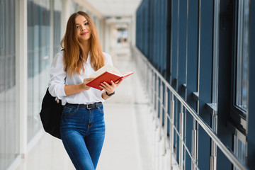 Portrait of a pretty female student with books and a backpack in the university hallway