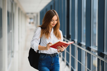 Positivity beautiful girl smiling at camera, standing on corridor with notes as backpack, going to lesson. Happy brunette female student studying in luxury university.