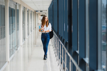 Cheerful brunette student girl with black backpack holds books in modern building. female student standing with books in college hallway