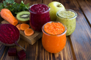 Different vegetable and fruit smoothies or puree in the small glass jars on the brown wooden  background. Closeup.