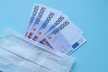 Medical protective surgical mask lies on money 500 euro banknotes on a blue background. Selective focus. Price increase for face masks