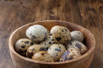 Obraz premium Close-up of wooden bowl with speckled quail eggs, with selective focus, on dark wooden table horizontal