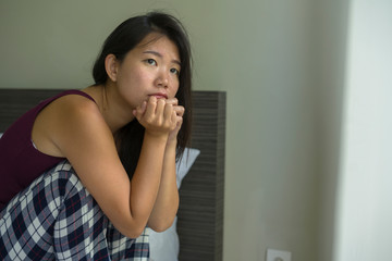 Fototapeta na wymiar lifestyle indoors portrait of young attractive sad and depressed Asian Chinese woman at home sitting on bed emotional and thoughtful feeling worried and scared about life problem