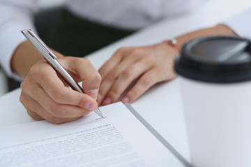 Female hand holding silver pen ready to make note in opened notebook sheet. Businesswoman coffee...
