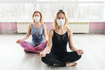 Two girls in medical masks do yoga in a closed Studio in sports clothes. Quiet meditation in the face of a virus epidemic. Group meditation