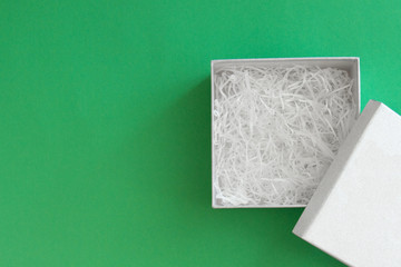 open box with cover with filling material inside lying on green colored paper background, top view with copy space