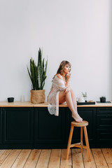 Morning breakfast, beautiful cute cute girl in home pajamas, dressing gown , making coffee sitting on the windowsill in a modern kitchen, weekend vacation, eco, freelance, comfort, spring