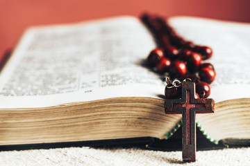 Close up Holy Bible and beads crucifix on a old round table. Beautiful red wall background.
