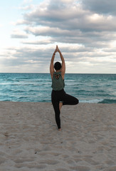  Attractive slim Woman doing yoga exercise on sandy beach, standing in Vrksasana Posture, Tree Pose, full length. Woman standing on one leg in yoga pose. Beautiful ocean on a background.Copy Space