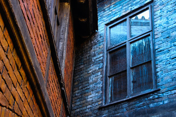 Corner of two old brick houses. Brick wall with messy window.