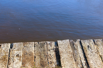 Aged wooden pier at the edge of water. Deck made of old wooden planks.