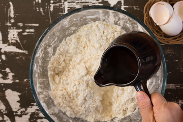 Woman hand holding ladle with hot water and pouring it into flour to make dough on brown background