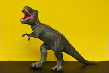 a toy Tyrannosaurus stands on a yellow background
