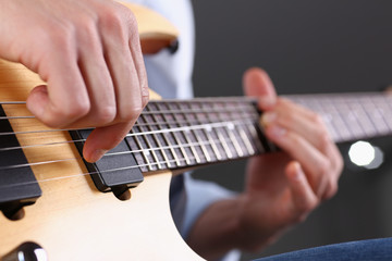 Male arms holding and playing classic shape wooden electric guitar closeup. Six stringed learning...