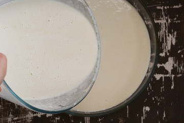 Top view of woman hand pouring semolina batter into form for baking mannik caressole on the brown background