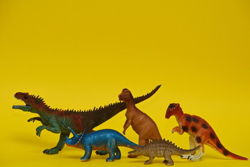 a group of toy dinosaurs walk on a yellow background