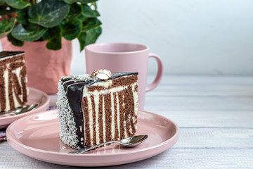 A slice of Zebra cake with chocolate icing. On a light background. In the background is a cup with floral tea.