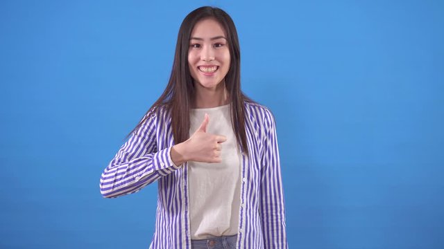 Positive young asian woman shows a thumbs up on a blue background