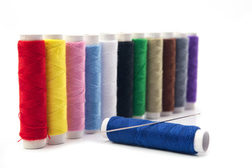 Colorful sewing thread rolls with needle on blue roll isolated on white background.Full dept of field. Craft concept.