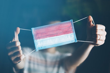 medical mask in hands of man, with the flag of Indonesia painted. Copy space