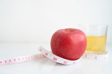 Apple and apple juice wrapped with measure tape  on white marble surface. Concept for fruit nutrition and diet food.