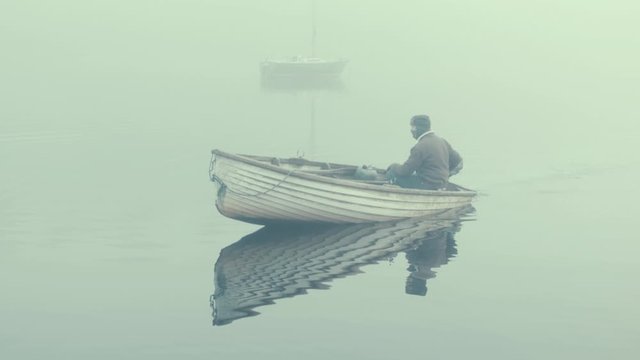 Man in fiberglass rowboat spins boat within fog
