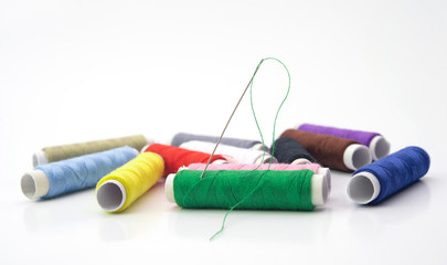 Colorful sewing thread rolls with needle on green roll isolated on white background.Full dept of field. Craft concept.