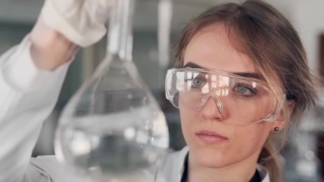 closeup portrait of female scientist examining liquid in test tube with magnifier