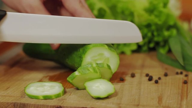 Close Image With Man Hands In Kitchen Cutting Flavored Cucumber in Fresh Slices for salad on a wooden board, side view. Healthy vegan food. Man on kitchen cooking natural and healthy meal.