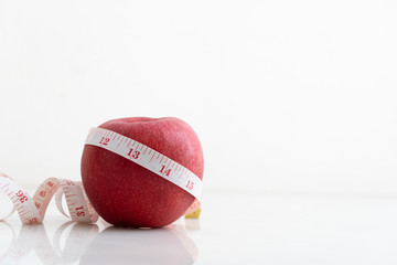 Apple wrapped with measure tape  on white marble surface. Concept for fruit nutrition and diet food.