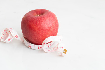 Apple wrapped with measure tape  on white marble surface. Concept for fruit nutrition and diet food.