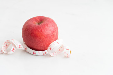 Apple wrapped with measure tape  on white marble surface. Concept for fruit nutrition and diet food.