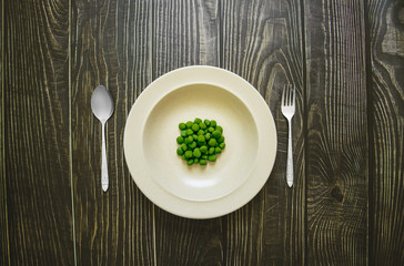 Green bean pea in plate with spoon and fork on wooden table