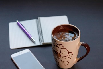 black background, coffee, notebook with pen and phone
