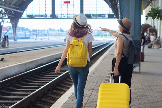 Two traveling women with suitcase backpacks walking along platform