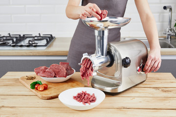 Raw meat. The process of preparing forcemeat by means of a meat grinder. Female hands use meat...