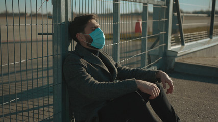 Fototapeta premium Sick man wearing Protective Face Mask sitting near fence border sneeze coughs COVID-19 coronavirus infection pandemic disease virus male tourist epidemic air health illness slow motion