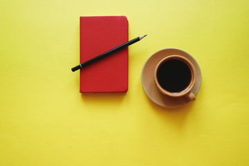 cup of coffee on yellow background with notepad