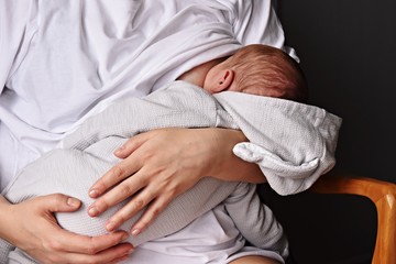 A mother is breastfeeding a baby sitting on a dark background. mother breast feeding and hugging her baby boy