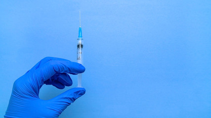 A syringe containing the coronavirus vaccine is held by a blue-gloved hand on a blue background in...