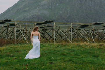 Fototapeta na wymiar Bride from back in white dress on green meadow, fish dryers on background