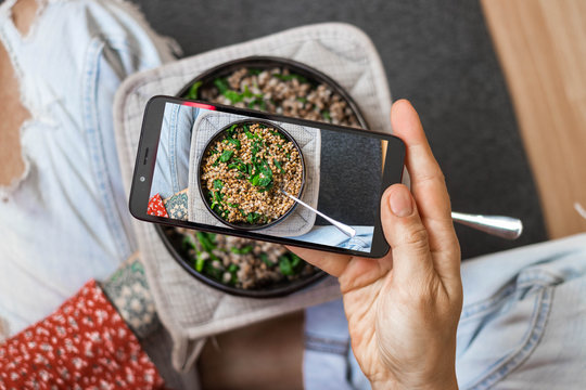 Make photo of buckwheat grain porridge with phone in woman hands. Smartphone food photography picture. Vegan, vegetarian healthy diet.