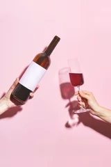 Foto op Aluminium Hands holding a glass of wine and a bottle on pink background. Glass of  wine in female hand. Party insta time. © Aliaksei