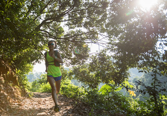 Young woman trail runner running on tropical forest trail during morning