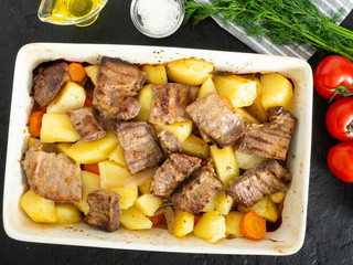 Fresh meat with vegetables and spices, cooked in the oven on a dark background.